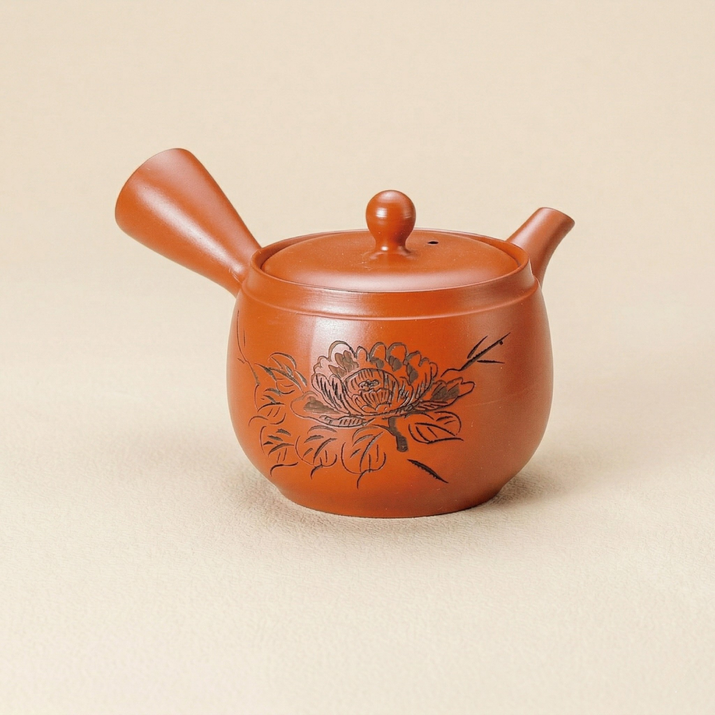 Red ceramic teapot with floral design on a beige background