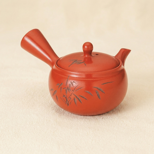 Red ceramic teapot with bamboo design on a beige background