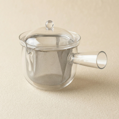 Clear glass teapot with a mesh filter on a beige background