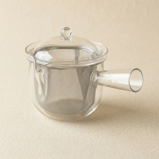 Clear glass teapot with a mesh filter on a beige background