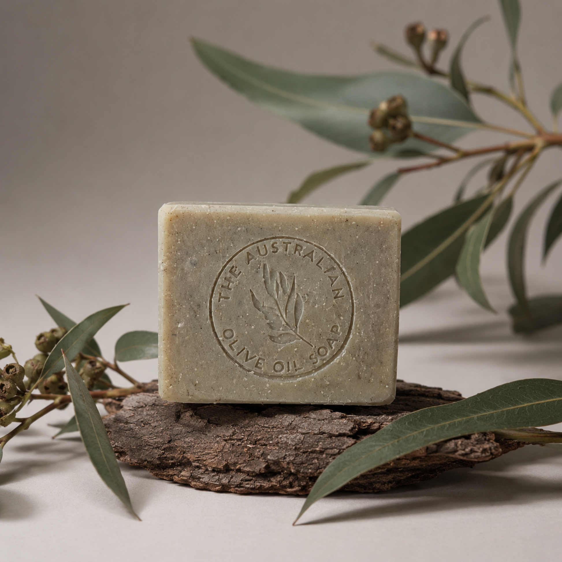 Bar of soap with a brand logo on a wooden block surrounded by eucalyptus leaves and branches.